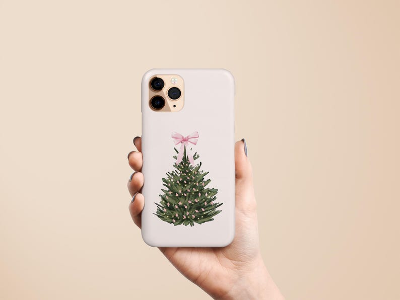 May include: A white phone case featuring a watercolor Christmas tree design. The tree is green with small white lights and a pink bow at the top. The case is held in a hand against a neutral background.