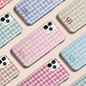 May include: A collection of phone cases with a gingham pattern in various colors, including pink, blue, and green. Each case features a monogram with initials. The cases are arranged on a light pink surface.