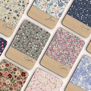 May include: A collection of personalized wooden coasters with floral patterns. Each coaster features a unique floral design in various colors, with a wooden base and a name in cursive script. The coasters are arranged in a grid.