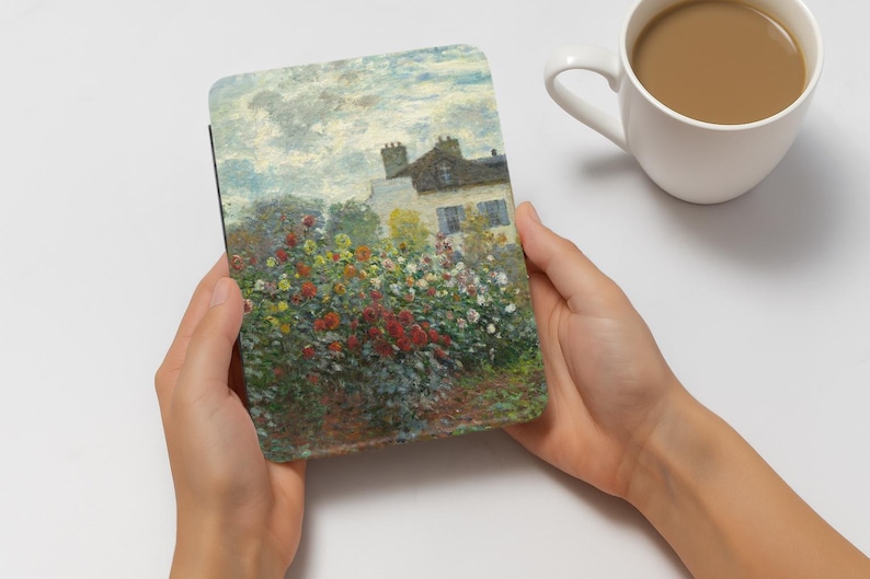 Może przedstawiać: Etui na tablet z kolorowym impresjonistycznym obrazem domu z ogrodem czerwonych, ż&oacute;łtych i białych kwiat&oacute;w. Etui trzymane jest w dw&oacute;ch dłoniach, z białym kubkiem kawy w tle.