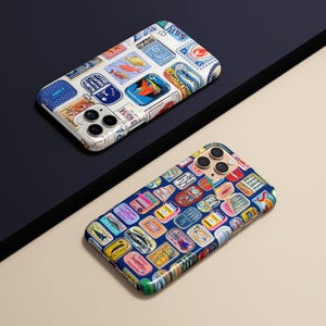 Może przedstawiać: Dwa etui na telefon z kolorowymi wzorami. Jedno etui ma białe tło z r&oacute;żnymi wzorami znaczk&oacute;w pocztowych. Drugie etui ma ciemnoniebieskie tło z kolorowymi wzorami znaczk&oacute;w pocztowych. Etui leżą na czarnej i beżowej powierzchni.