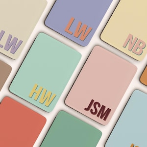 May include: A selection of pastel-coloured rectangular items, each displaying initials. The colours include beige, lavender, yellow, mint green, pink, and orange. The initials are in contrasting colours, such as purple, orange, and brown.