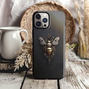 May include: A black phone case with a steampunk-style bee design. The bee is made of gold and silver metal and has intricate details. The case has a dark background and a subtle texture.