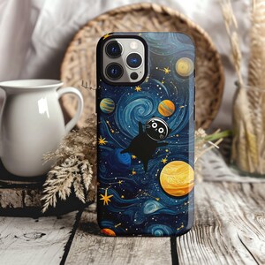 May include: A black phone case with a galaxy-themed design. The case features a black cat floating in space with planets and stars in the background. The case has a blue, yellow, and white color scheme.