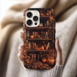 May include: A phone case featuring a detailed illustration of a bookshelf decorated for autumn. The design includes pumpkins, fall leaves, books, and a lit candle, creating a cozy, seasonal aesthetic.