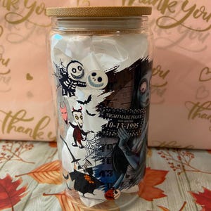 May include: A clear glass tumbler with a bamboo lid features a colorful graphic print of characters from the Nightmare Before Christmas movie. The print includes Jack Skellington, Sally, Oogie Boogie, and other characters. The text "Nightmare Police" and "10-13-1995" is visible on the print.