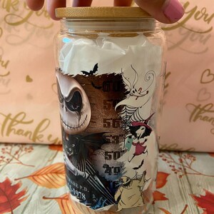 May include: A glass jar with a bamboo lid featuring a Nightmare Before Christmas design. The jar has a black and white image of Jack Skellington, Sally, and Zero. The jar also has a measurement scale on the side.