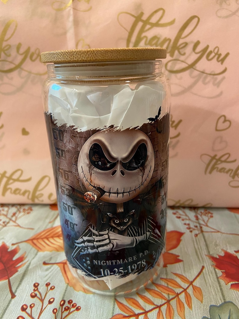 May include: A glass jar with a bamboo lid featuring a graphic of Jack Skellington from The Nightmare Before Christmas. The graphic shows Jack Skellington smoking a cigar and holding a cat. The text "Nightmare P.D. 10-25-1978" is printed on the jar.