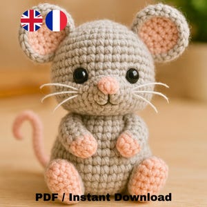 May include: A handmade crocheted mouse in grey with pink detailing on the ears, nose, paws, and tail. It has black eyes and white whiskers. The image includes the text "PDF / Instant Download". This is a craft item.