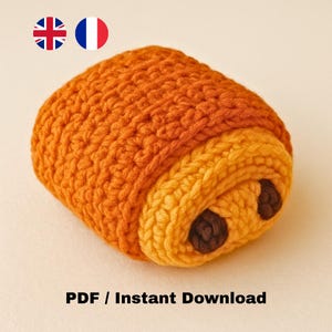 Peut inclure: Un pain au chocolat crocheté aux tons orange et jaune. L'article fait main présente une surface texturée et deux accents marron foncé ressemblant à du chocolat. Le texte "PDF / Téléchargement instantané" est en bas.