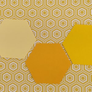 May include: Three yellow and orange hexagon shapes on a yellow and white honeycomb pattern background. The hexagons are in shades of light yellow, orange, and bright yellow. The background pattern is a repeating geometric design.