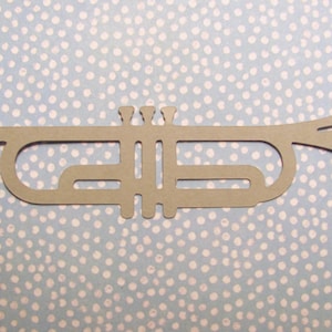 May include: A brown paper cutout of a trumpet on a blue background with white polka dots.