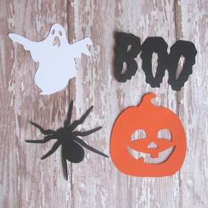 May include: A set of Halloween decorations featuring a white ghost, a black spider, an orange pumpkin with a jack-o'-lantern face, and a black paper cutout of the word "BOO".