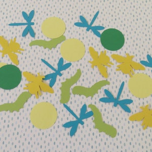 May include: A collection of paper cutouts featuring yellow bees, blue dragonflies, and green and yellow circles. The cutouts are arranged on a white background with a blue polka dot pattern.
