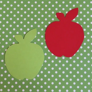 May include: Two paper apples, one red and one green, on a green background with white polka dots.