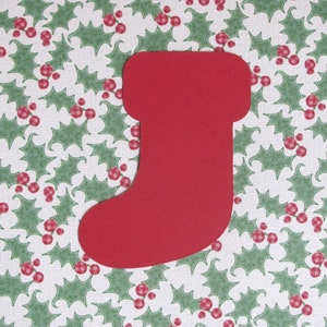 May include: A red paper stocking cutout on a white background with a green holly leaf pattern.