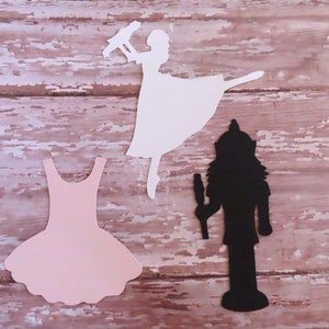 May include: Three paper cutouts: a white ballerina silhouette holding a bird, a pink tutu, and a black silhouette of a nutcracker.