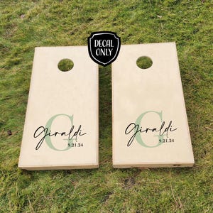 K&ouml;nnte beinhalten: Zwei h&ouml;lzerne Cornhole-Bretter mit einem gr&uuml;nen und schwarzen Aufkleber, auf dem "Giraldi 9.21.24" steht.