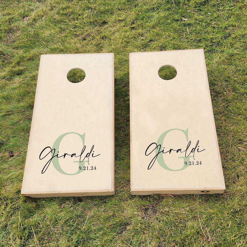 K&ouml;nnte beinhalten: Zwei h&ouml;lzerne Cornhole-Bretter mit einem gr&uuml;n-schwarzen Design. Die Bretter sind mit dem Namen "Giraldi" und dem Datum "9.21.24" personalisiert.