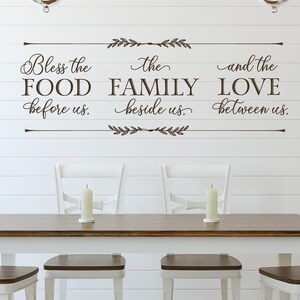 May include: A white wall with a brown vinyl decal that reads "Bless the food before us. The family beside us. And the love between us."