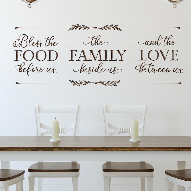 May include: A white wall with a brown vinyl decal that reads "Bless the food before us. The family beside us. And the love between us."