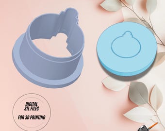 Peut inclure: Un emporte-pièce imprimé en 3D en forme de boule de Noël. L'emporte-pièce est bleu clair et a une surface lisse et arrondie. L'image montre également un rendu numérique de l'emporte-pièce, qui est un cercle bleu clair avec un cercle plus petit découpé au centre. Le texte "DIGITAL STL FILES FOR 3D PRINTING" est visible sur l'image.
