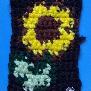 Peut inclure: Gros plan sur un petit tournesol crocheté avec un centre brun et des pétales jaunes. Le tournesol est sur un fond noir avec une feuille verte.