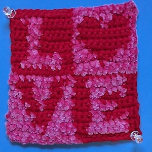 May include: A red and pink crocheted square with a textured pattern. The square is made with a combination of red and pink yarn, creating a unique and visually appealing design.