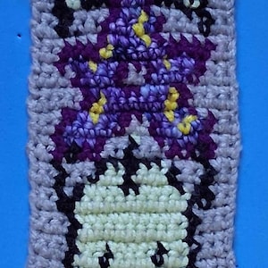 May include: A crocheted square with a purple flower design and a white skull with black eyes and a purple mouth.