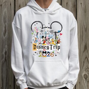 A person wearing a white hoodie with a graphic design featuring Disney characters and the text "Disney Trip 2026".