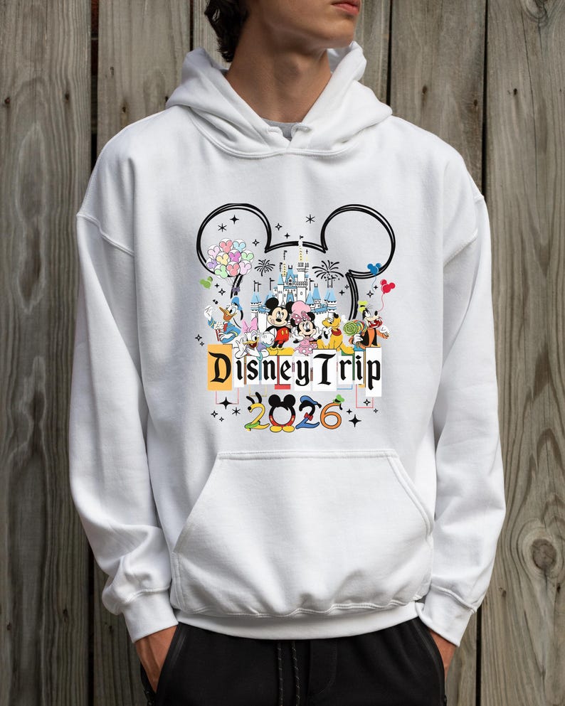 A person wearing a white hoodie with a graphic design featuring Disney characters and the text "Disney Trip 2026".