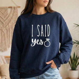 A woman wearing a navy blue sweatshirt with the text "I SAID YES" printed on it.