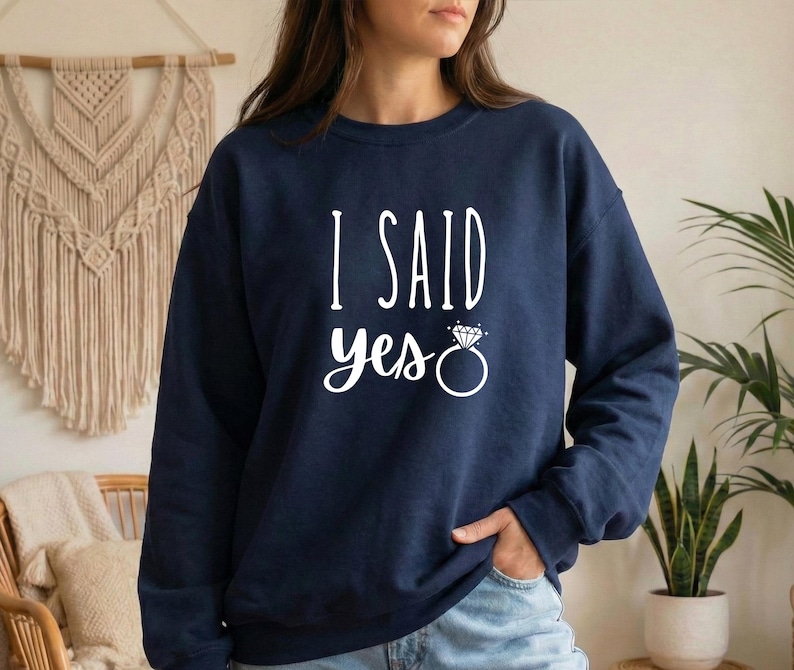 A woman wearing a navy blue sweatshirt with the text "I SAID YES" printed on it.