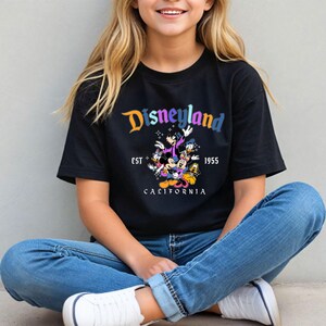 A smiling young woman wearing a black t-shirt with a Disneyland graphic and text, sitting on the ground.