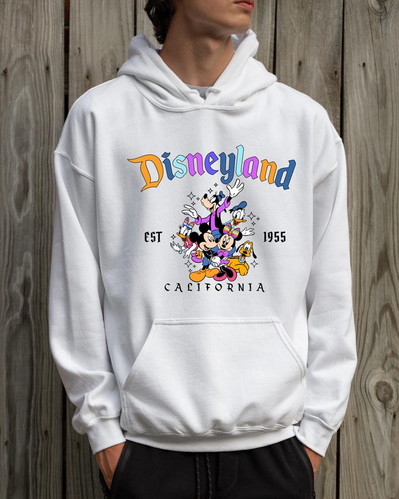 A person wearing a white hoodie with a graphic of Disney characters and text that says "Disneyland California".