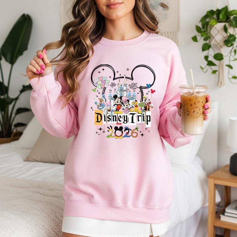 A woman wearing a pink sweater with a Disney-themed design and holding a drink in a glass.