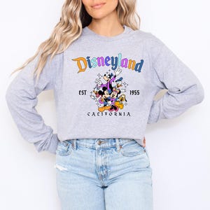 A woman wearing a gray sweatshirt with a Disneyland graphic and text, along with a graphic of Disney characters.