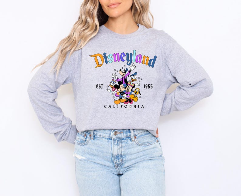 A woman wearing a gray sweatshirt with a Disneyland graphic and text, along with a graphic of Disney characters.