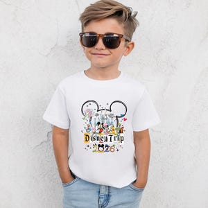 A young boy wearing a white t-shirt with a Disney-themed graphic and sunglasses, smiling at the camera.