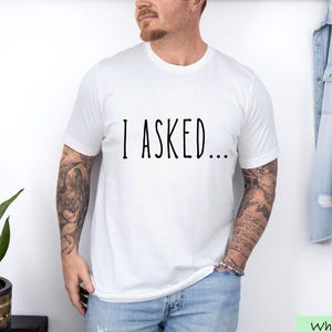 A man wearing a white t-shirt with the text "I asked..." standing in front of a denim jacket.