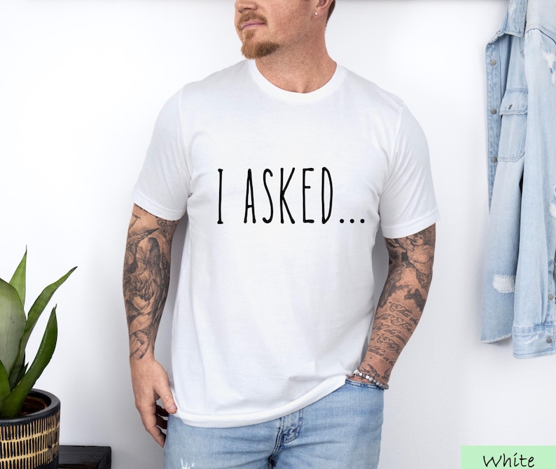 A man wearing a white t-shirt with the text "I asked..." standing in front of a denim jacket.