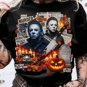 Puede incluir: Camiseta negra con un diseño de Halloween que presenta a Michael Myers, un cuchillo y una calabaza tallada. El diseño incluye elementos de texto como "Murder", "Boogeyman Massacre" y "The Night He Came Home."