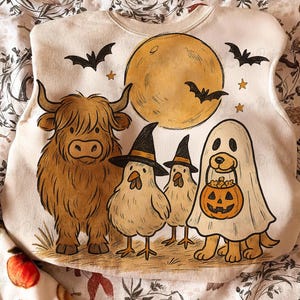 May include: Cream-coloured Halloween-themed sweatshirt featuring a Highland cow, two chickens in witch hats, and a dog in a ghost costume. A full moon, bats, and stars complete the design. The illustration is in a cartoon style.