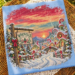 May include: A rectangular fabric print featuring a snowy Whoville scene with a wooden sign reading Whoville Est. 1957. The illustration displays colourful, curved buildings, snow-covered pine trees with red bows, a stone bridge, and a sunset sky.