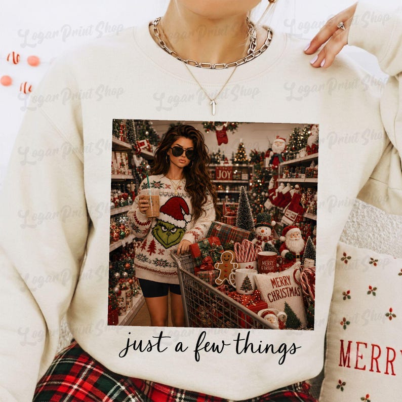 May include: A cream-colored crewneck sweatshirt featuring a graphic print of a person wearing a Grinch sweater and holding a drink in a store aisle filled with Christmas decorations. The text "just a few things" is printed below the graphic.