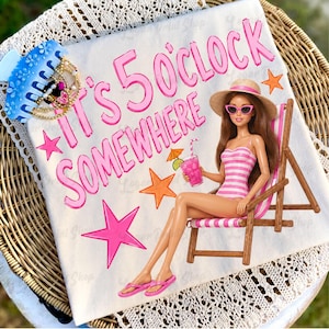 Puede incluir: Una toalla de playa blanca con la frase "It's 5 O'Clock Somewhere" en letras rosas. Una muñeca Barbie con un traje de baño a rayas rosas y blancas está sentada en una silla de playa, sosteniendo una bebida rosa. La toalla está decorada con estrellas rosas y naranjas.
