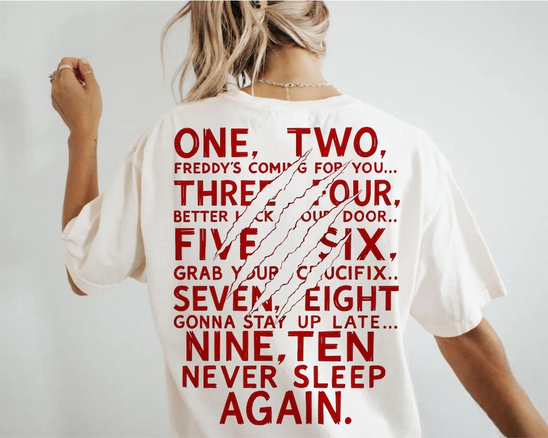 May include: Cream-colored t-shirt with red text and claw marks. The text reads "ONE, TWO, FREDDY'S COMING FOR YOU... THREE FOUR, BETTER LOCK YOUR DOOR..." and continues with the numbers five through ten. A horror-themed graphic tee.