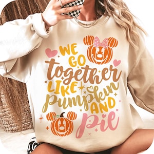 以下が含まれることがあります： 様々な色で「We go together like pumpkin and pie」と書かれたベージュのスウェットシャツ。デザインには、カボチャの形をしたミッキーマウスの頭とハートが含まれており、秋とハロウィーンに最適です。