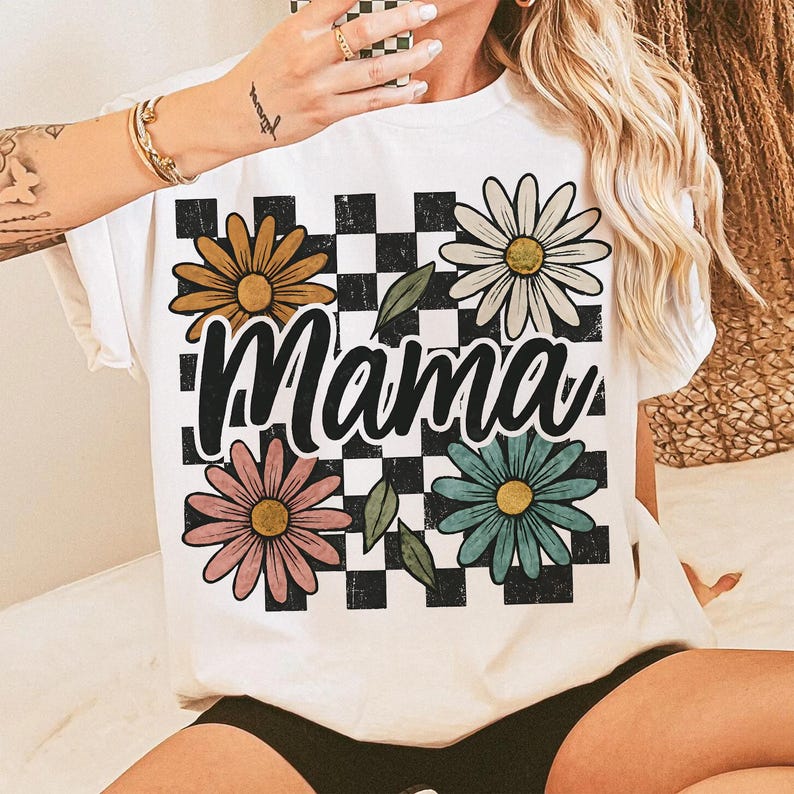 May include: White t-shirt with a black and white checkered pattern, four colorful daisies, and the word "Mama" in a black script font.