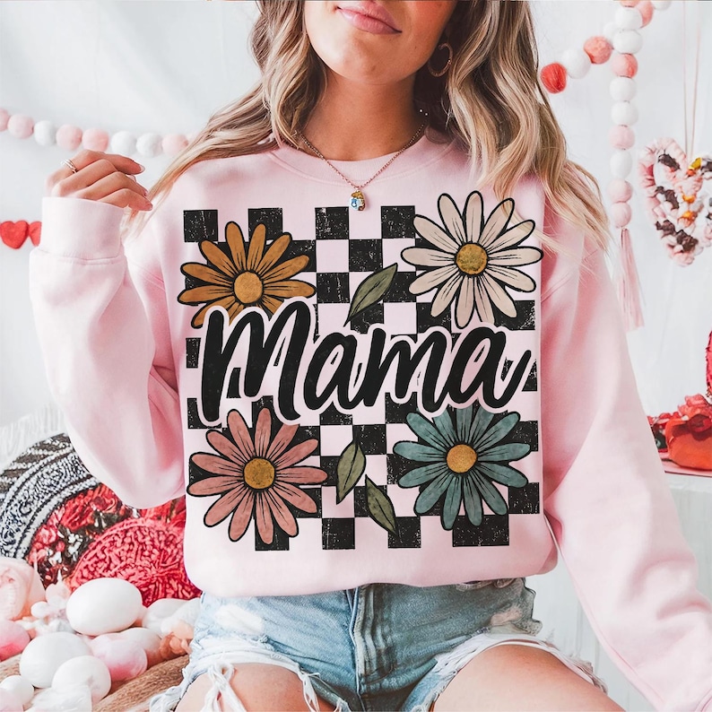 May include: Pink sweatshirt with a black and white checkered pattern, four colorful daisies, and the word "Mama" in a black script font.